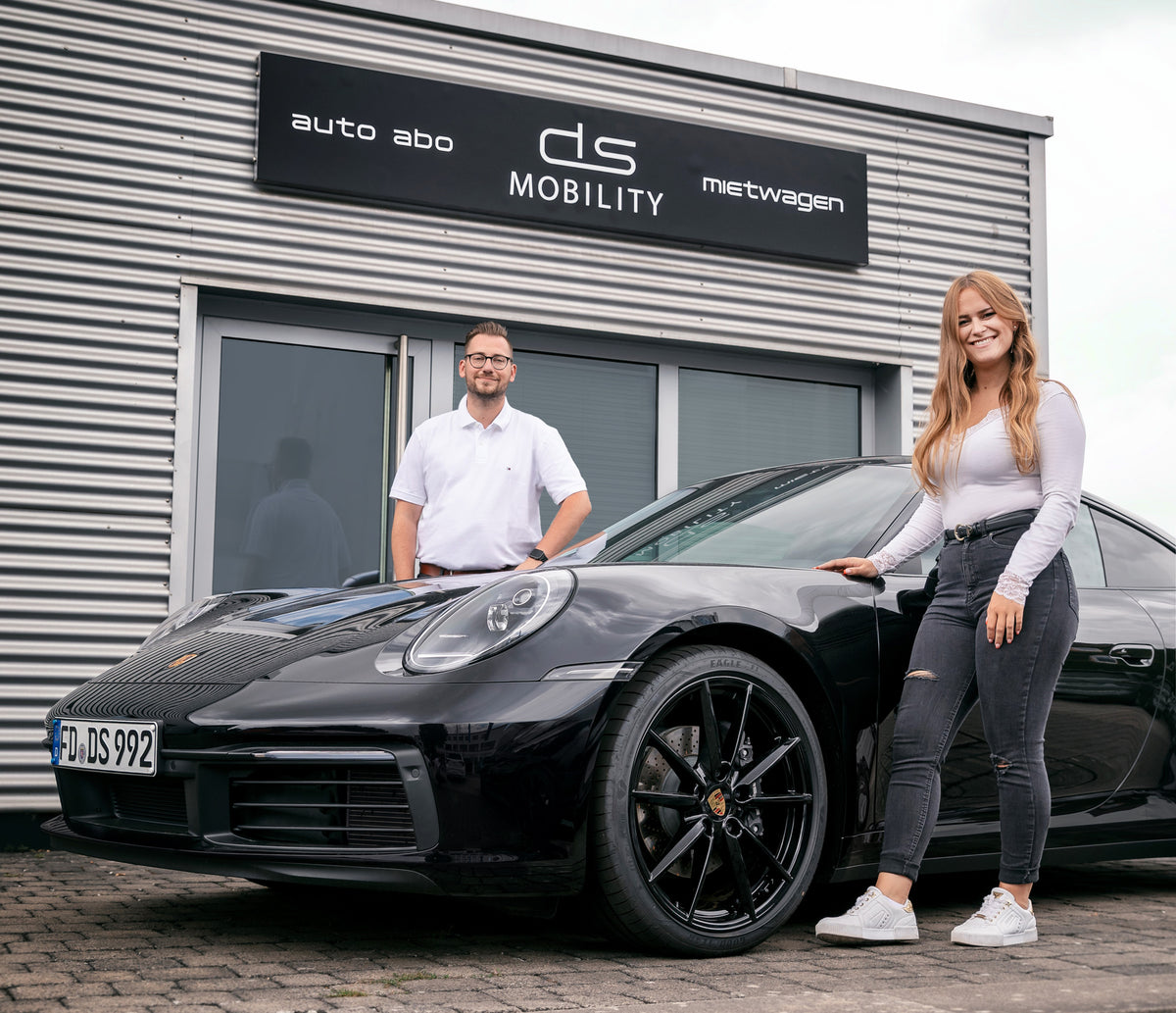 Das DS Mobility Team vor ihrem Büro mit einem schwarzen Porsche 911